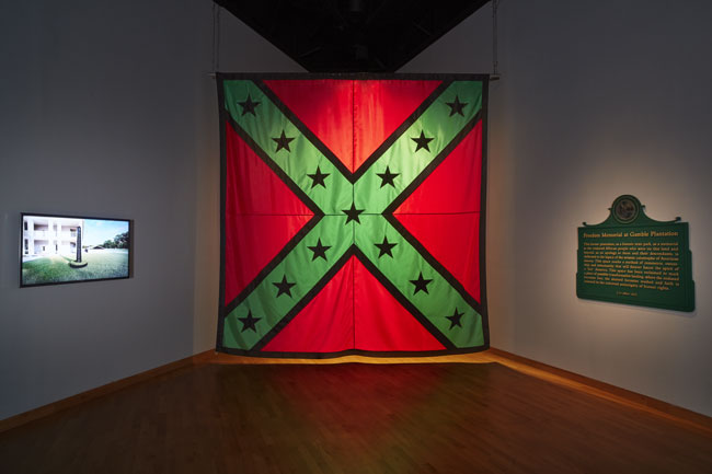 Left to right: John Sims, Freedom Memorial at Gamble Plantation, 2020. 7:00 min. video animation with sound; John Sims, AfroConfederate Flag: 12 Foot, 2020. Nylon; John Sims, Freedom Memorial Marker, 2020. Latex paint on synthetic material. All works Courtesy of the artist.